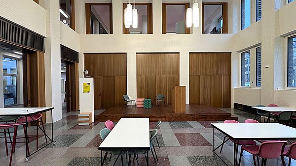 Kassenhalle mit Bühne, Tischen und Stühlen.