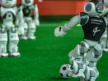 Robots on a playing field. The one on the right kicks the ball.