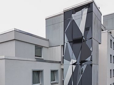 Wandbild an einer Hausfassade mit symmetrischen, grauen Formen.
