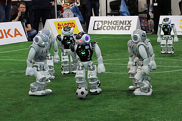 Ein B-Human-Roboter dribbelt durch das Mittelfeld und passiert einige Roboter der Bembelbots aus Frankfurt.