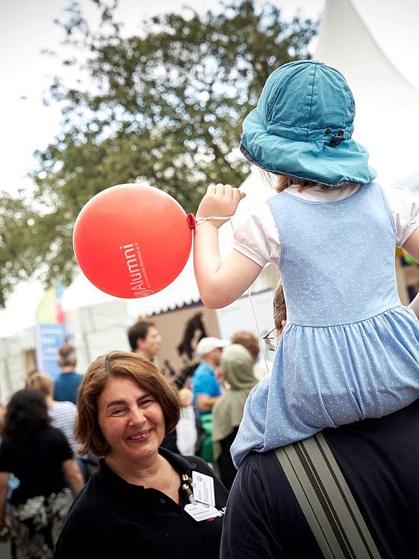AUfnahme vom Open Campus 2024. Mauela lächelt einem Kind zu das auf der Schulter eines Erwachsenes sitzt