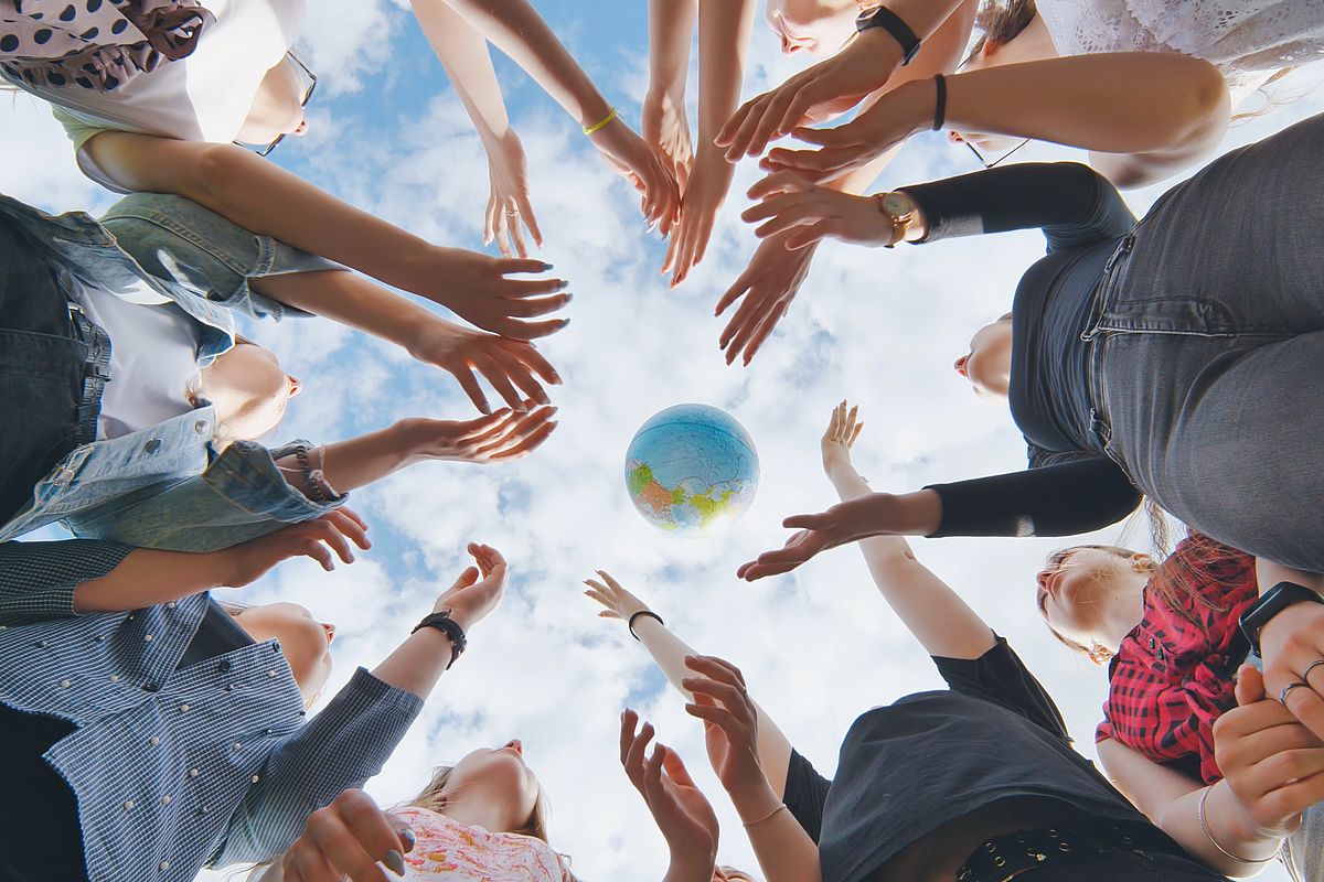 Menschen werfen eine Weltkugel in die Luft