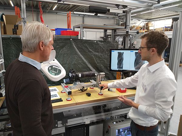 Two persons standing in front of a table with an image capture device on it