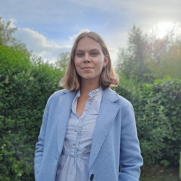 Junge Frau in blau gekleidet vor grüner Landschaft und klarem Himmel bei Sonnenschein