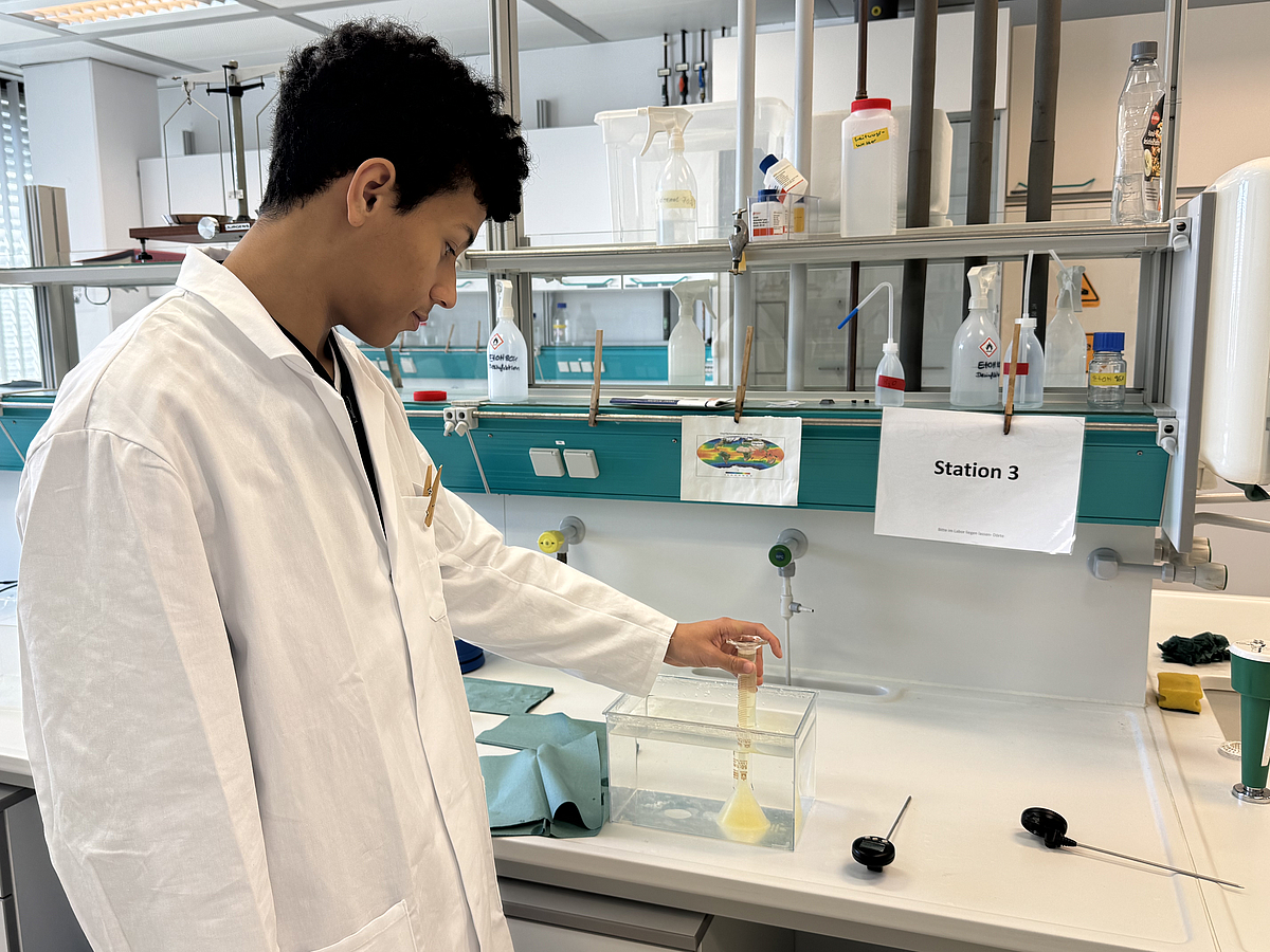 CO2-Löslichkeit in Wasser Ein Schüler in Kittel steht an einer Laborbank betrachtet einen Versuch zur CO2-Löslichkeit in Wasser.