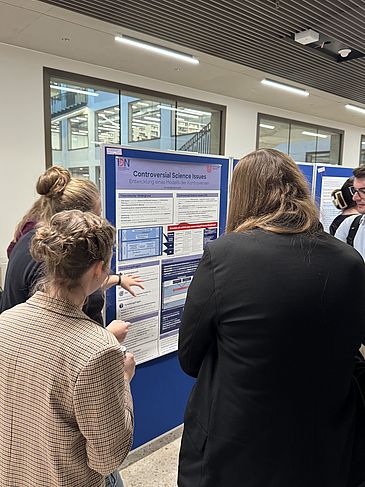 Mehrere Personen diskutieren an einem wissenschaftlichen Poster.