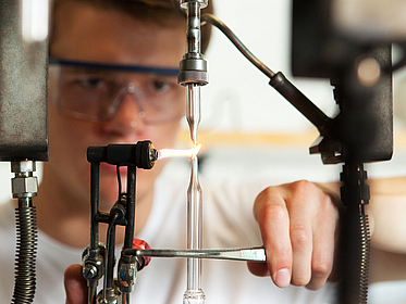 Eine Person im Labor bei der Arbeit mit einem Bunsenbrenner.