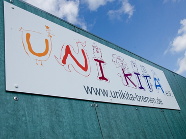 Logo des Uni-Kita e. V. an der Wand des Kita-Gebäudes.