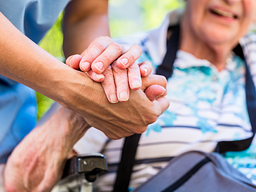 Pflegeperson hält die Hand einer Seniorin