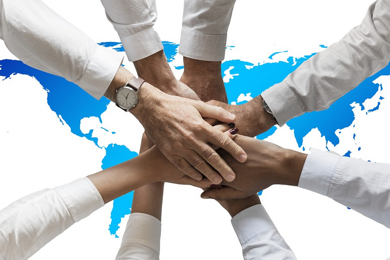 Viele Händen liegen übereinander als Zeichen von Kooperation - eine Weltkarte im Hintergrund