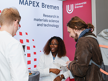 Zwei MAPEX Doktorand:innen sprechen mit einem Teilnehmenden der Messe Die Praxisbörse.