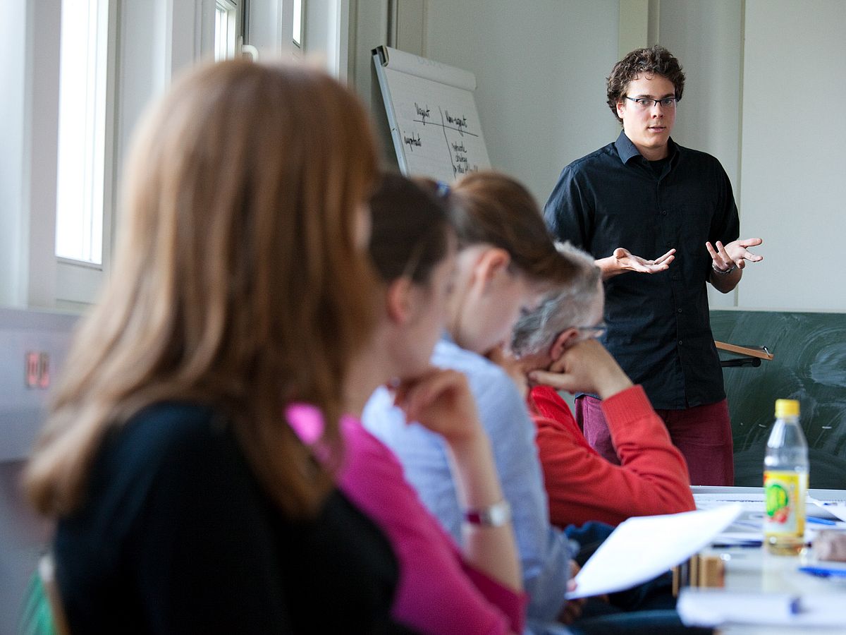 Ein Lehrender vor einer Gruppe von Zuhörern in einem Seminarraum.