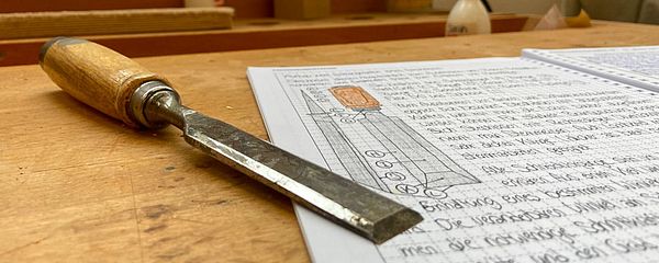 A neatly written sheet of paper and a tool lie on a wooden workbench.