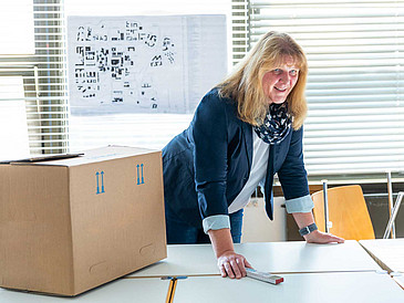 Heike Hemmersbach leans over a table, in the background a room plan