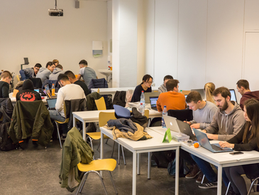 Studierende sitzen in Gruppen zusammen und arbeiten an Laptops