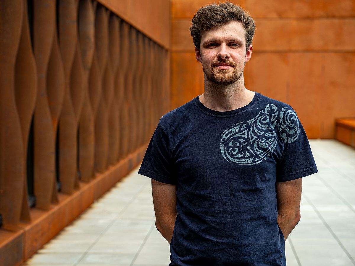 Ilya Bobrovskiy is standing with his arms crossed behind his back in front of a rust-red wall.