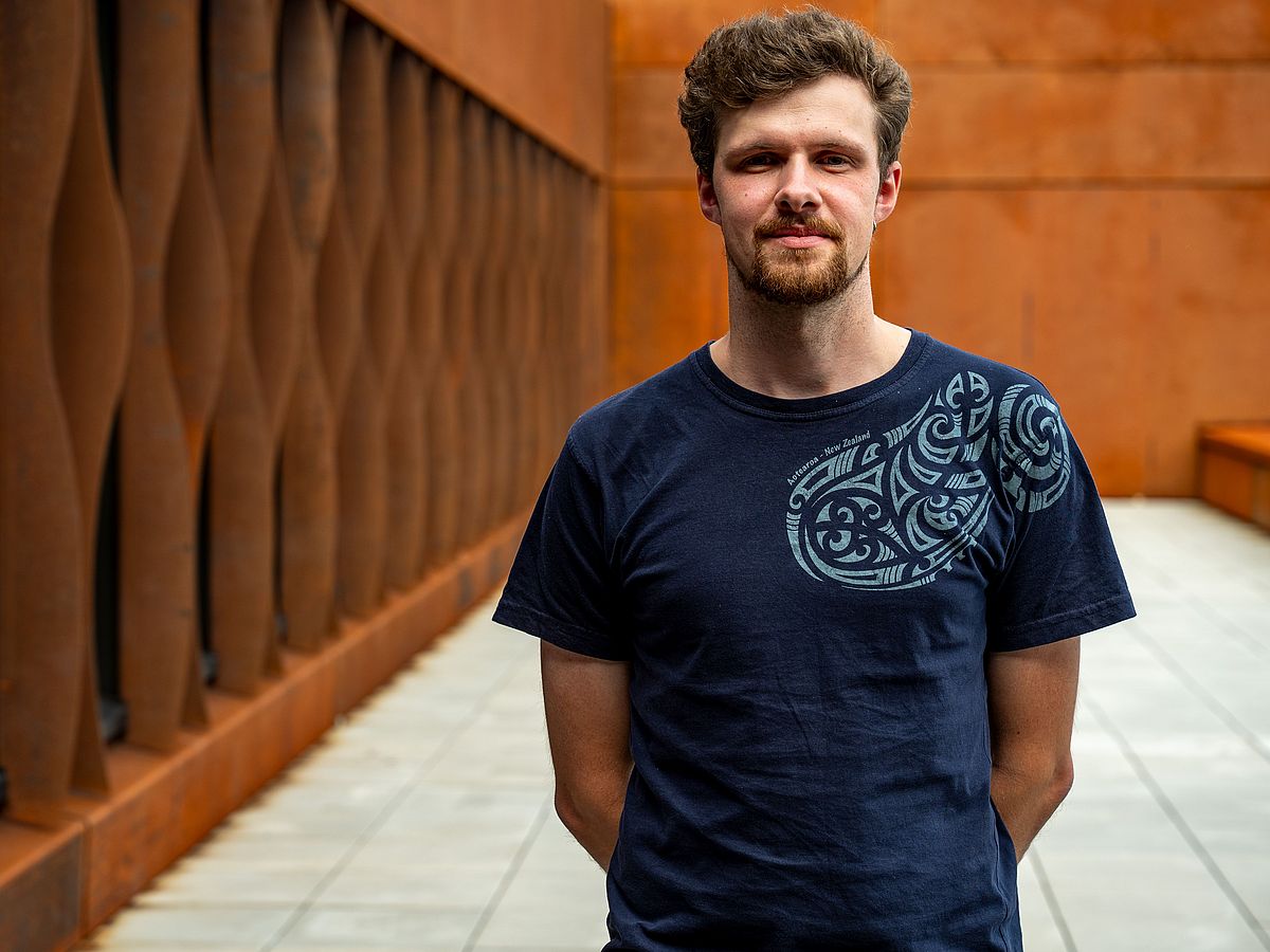 Ilya Bobrovskiy steht mit den Armen hinter dem Körper verschränkt vor einer rostroten Wand.