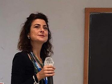 Alice Lemmo hält ein Mikrofon in der Hand und scheint jemandem zuzuhören, wahrscheinlich im Kontext einer Tagung