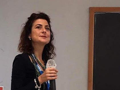 Alice Lemmo hält ein Mikrofon in der Hand und scheint jemandem zuzuhören, wahrscheinlich im Kontext einer Tagung