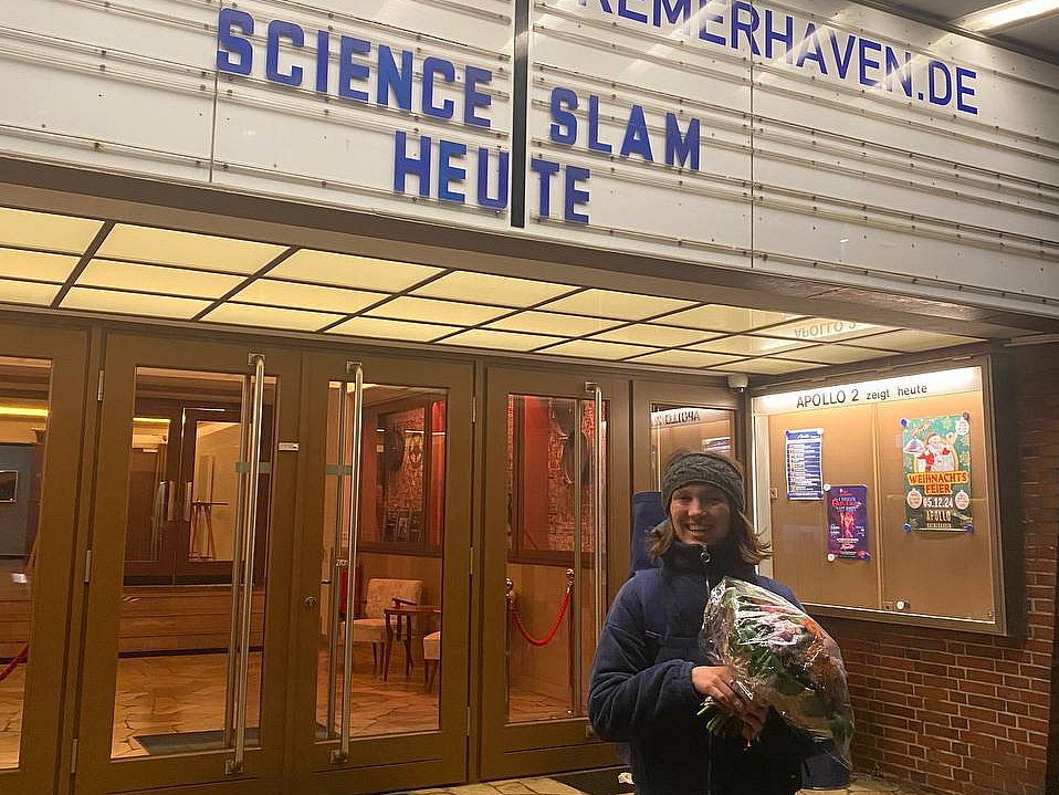 Eine Frau steht vor einem Kino in Bremerhaven mit einem Blumenstrauß.