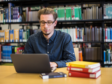Ein Studierender arbeitet in der Bibliothek am Laptop.