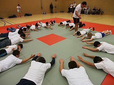 Sportler liegen bäuchlings im Kreis auf dem Boden.