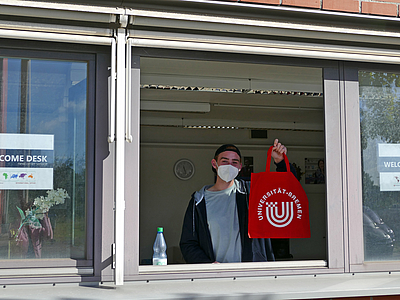 Studen zeigt roten Uni-Beutel aus dem Fenster