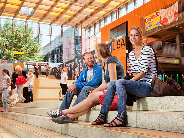 Studierende sitzen auf der Treppe in der Glashalle