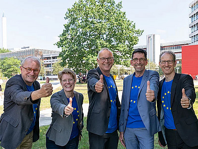 Director of Finance and Administration Martin Mehrtens, Vice President Eva Feichtner, President Bernd Scholz-Reiter, and Vice Presidents Thomas Hoffmeister and Andreas Breiter infront of the MZH Building. They all wear t-shirts with the European flag and give a thumbs up.