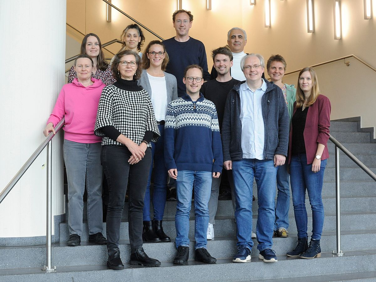 12 Menschen stehen auf einer Treppe und schauen freundlich in die Kamera