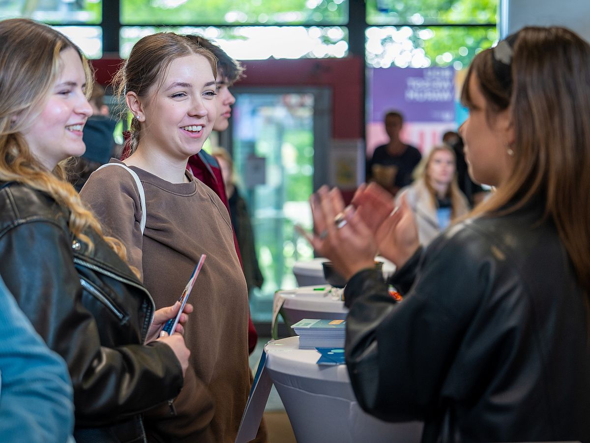 Eine Studierende und Studieninteressierte stehen um einen Stehtisch mit Infomaterialien.