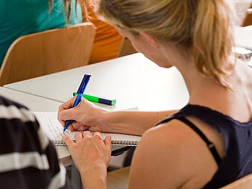 Eine Studierende macht sich in einem Seminarraum Notizen.