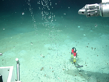 Ein Greifarm eines Tauchroboters setzt einen Sensor in den Meeresboden.