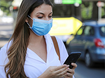 Young woman with mouth-nose covering looks at her smartphone.